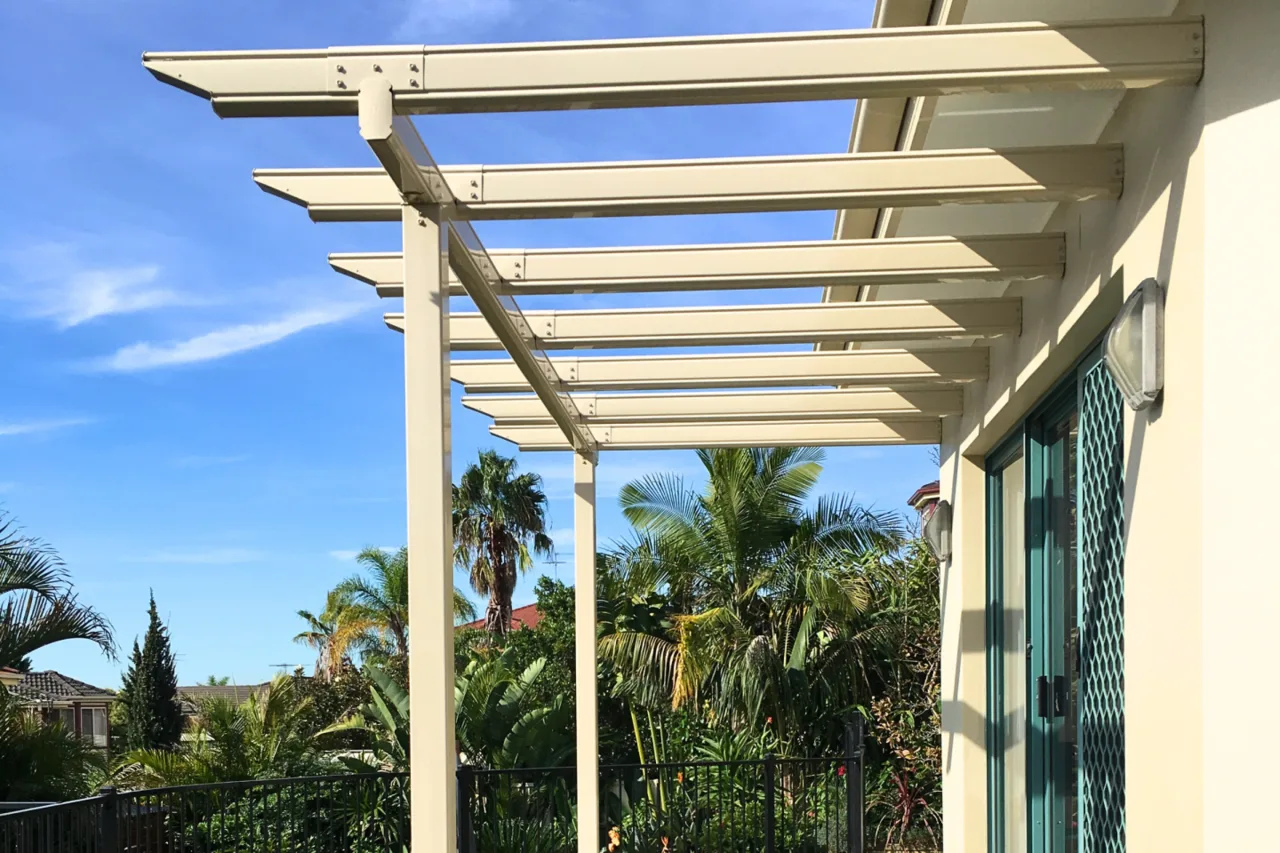 Cream skillion pergola attached to a rendered home beside tropical planting — Sutherland, NSW